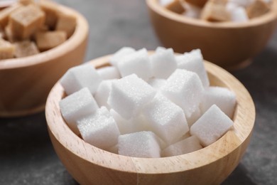 Different sugar cubes in bowls on table, closeup