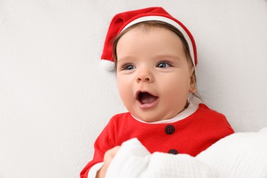 Photo of Cute baby wearing festive Christmas costume on white bedsheet, top view