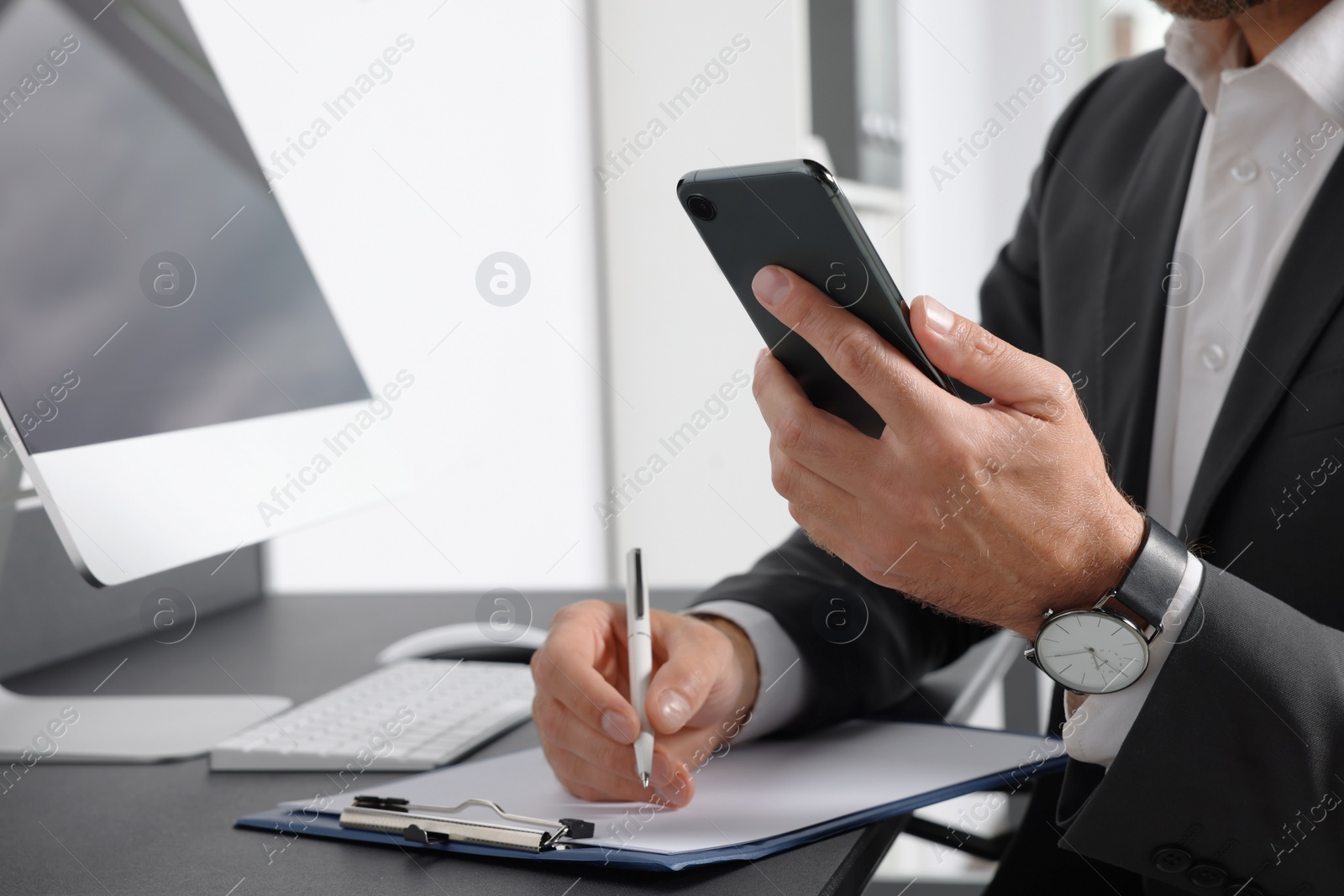 Photo of Handsome man using smartphone while working at table in office, closeup