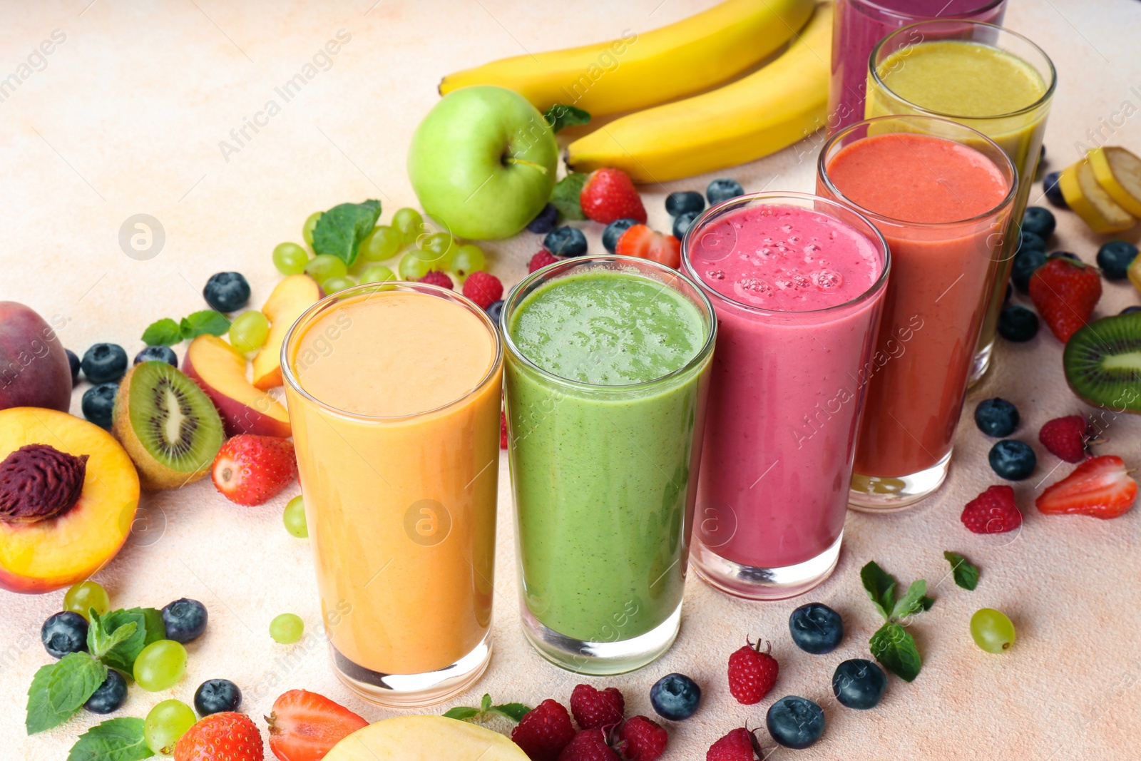 Photo of Fresh colorful fruit smoothies and ingredients on beige table