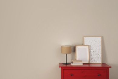 Photo of Red chest of drawers with lamp, books, picture and photo frame near light wall, space for text. Interior design