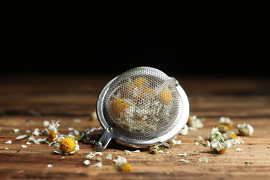 Photo of Dry chamomile flowers in infuser on wooden table, closeup