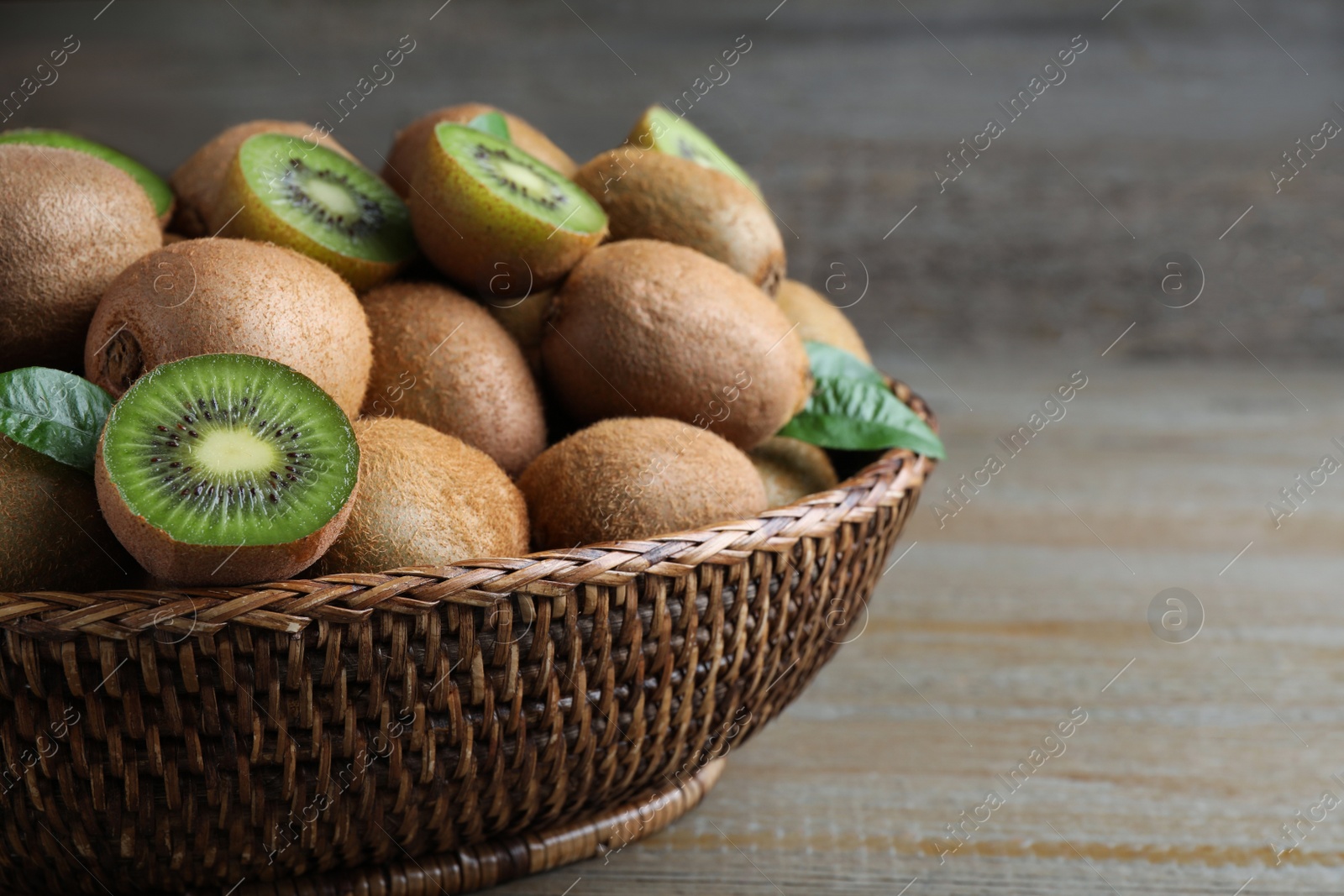 Photo of Fresh ripe kiwis in wicker bowl on wooden table, closeup. Space for text