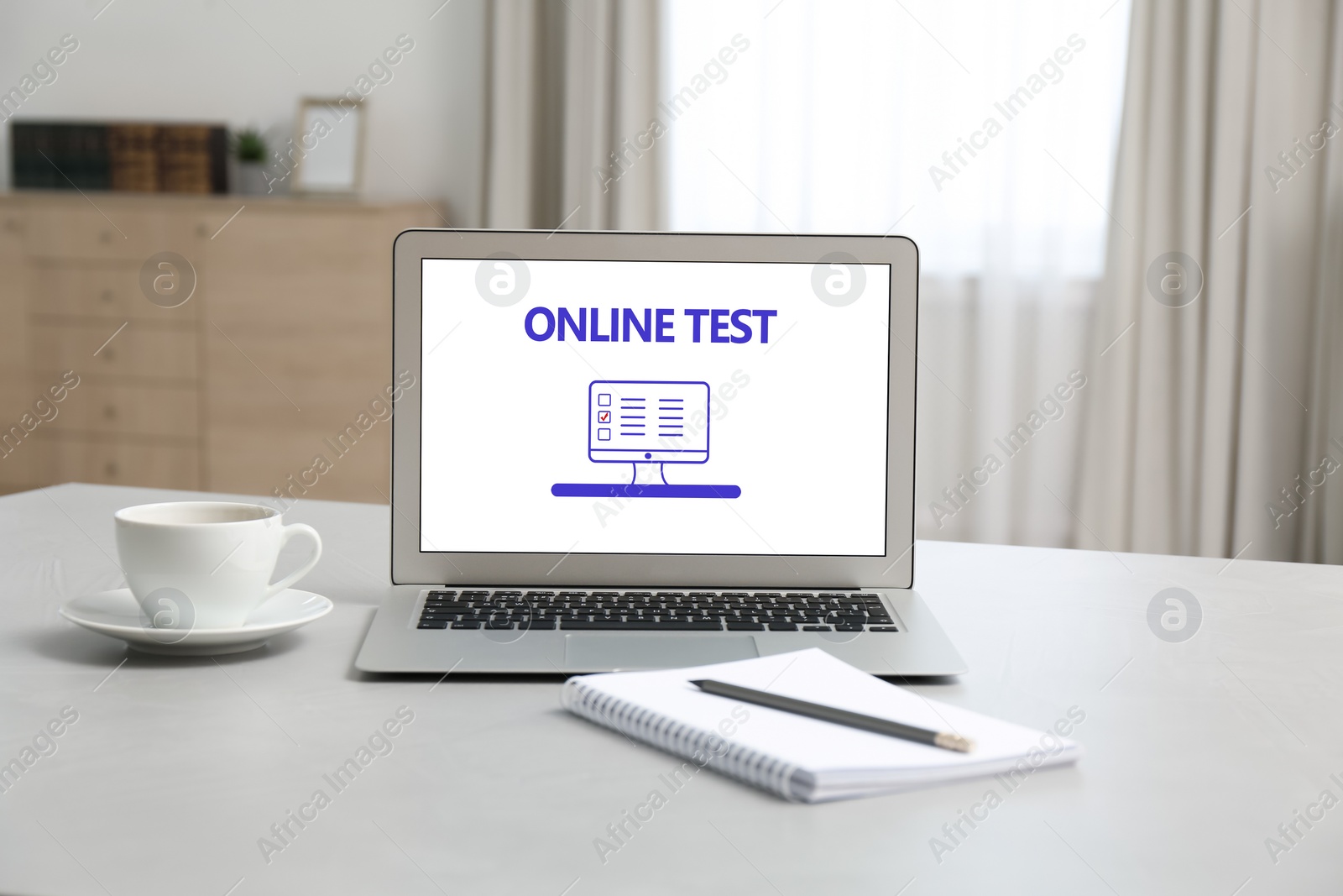 Photo of Laptop with online test, notebook and cup of coffee on table at home