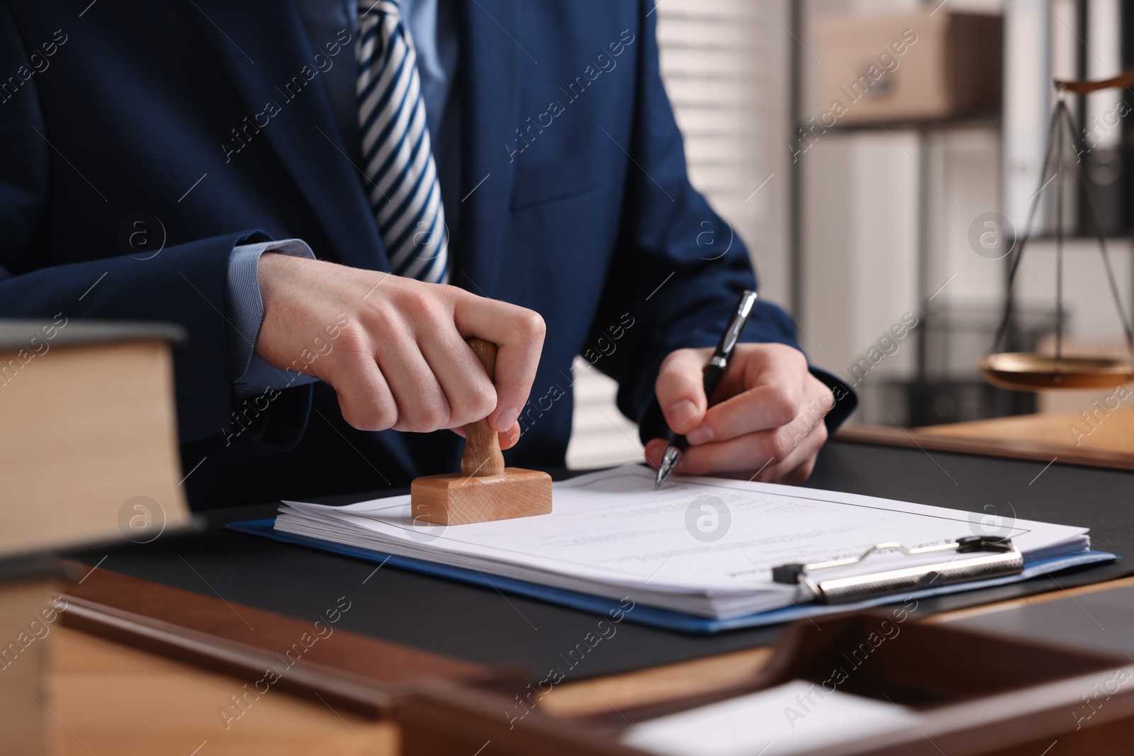 Photo of Notary with pen stamping document at table in office, closeup