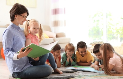 Young woman reading book to little children indoors. Learning by playing