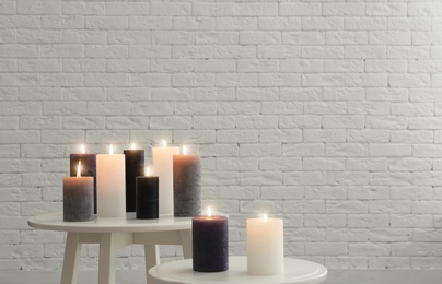 Burning candles on tables against brick wall with space for text