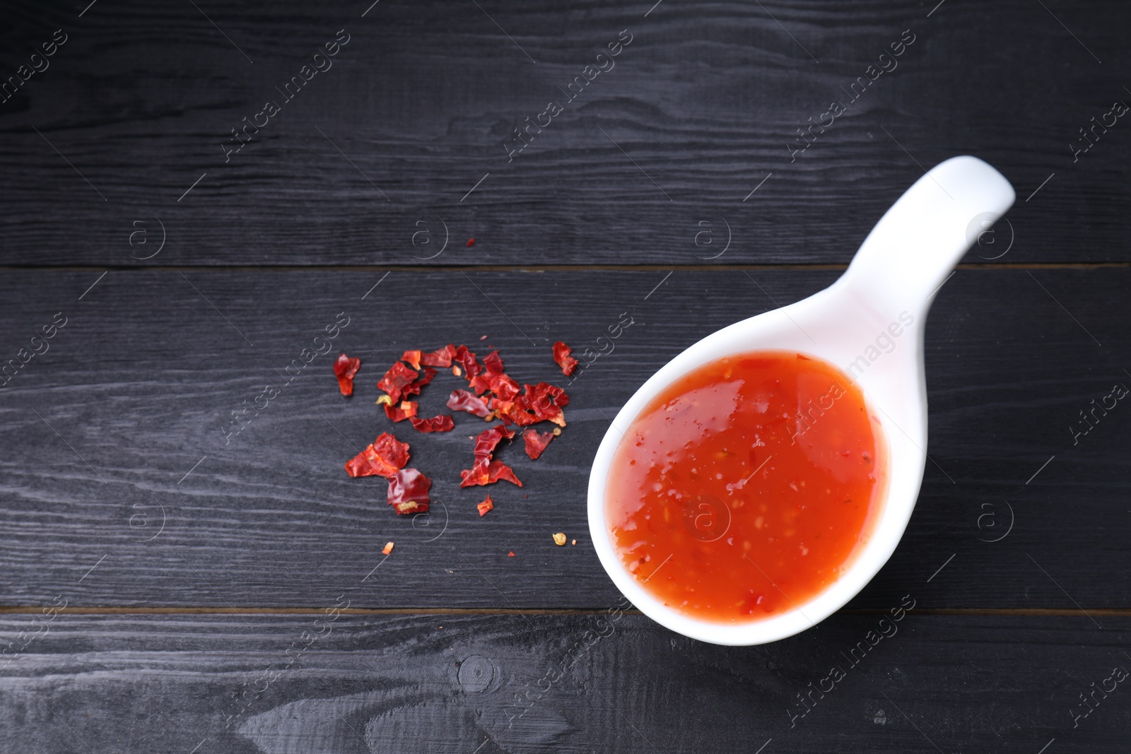 Photo of Chili sauce in spoon on black wooden table, top view