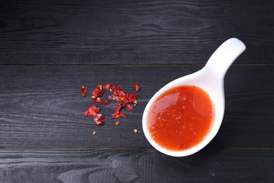 Photo of Chili sauce in spoon on black wooden table, top view