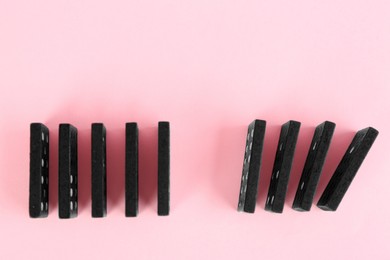 Photo of Black domino tiles on pink background, flat lay. Space for text