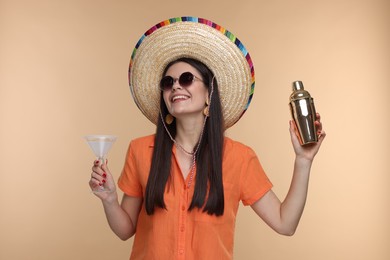 Young woman in Mexican sombrero hat with cocktail and shaker on beige background