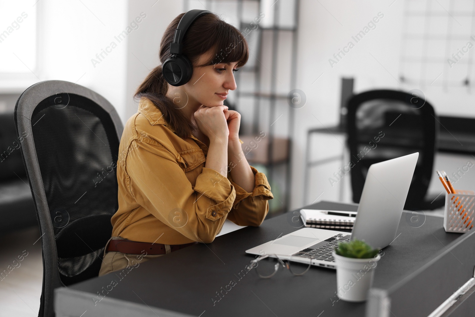 Photo of Woman in headphones watching webinar at table in office