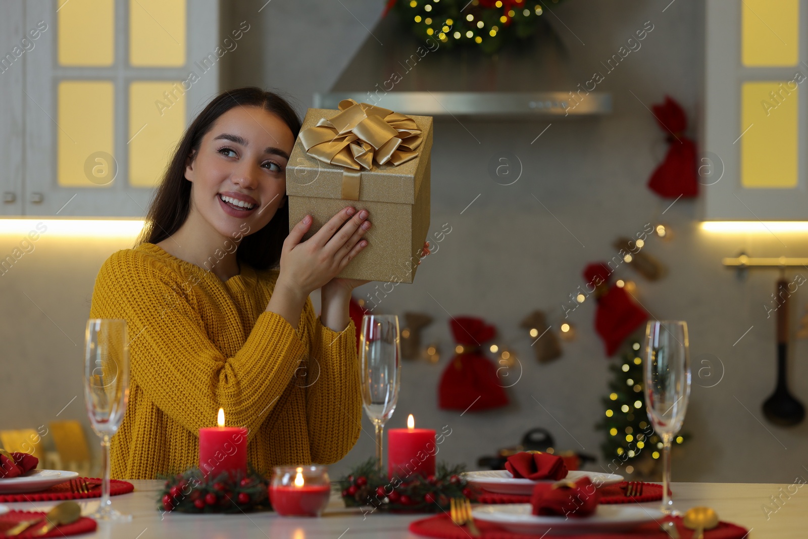 Photo of Happy young woman with Christmas gift at table in kitchen