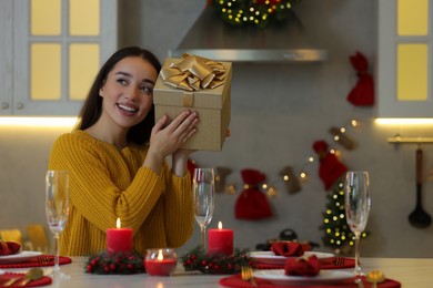 Photo of Happy young woman with Christmas gift at table in kitchen