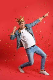 Photo of Happy man in party crown and confetti on red background