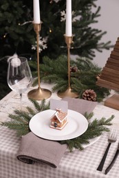 Festive place setting with beautiful dishware, cutlery and gingerbread house card holder for Christmas dinner on checkered tablecloth, above view