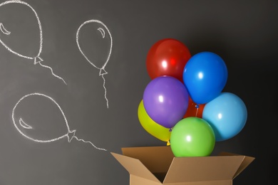 Gift box with bright air balloons and chalk drawing on grey background