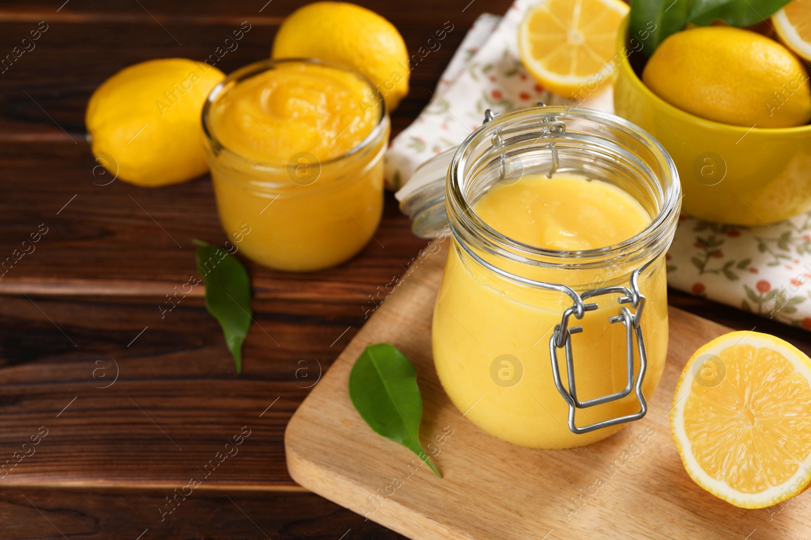 Photo of Delicious lemon curd in glass jars, fresh citrus fruits and green leaves on wooden table