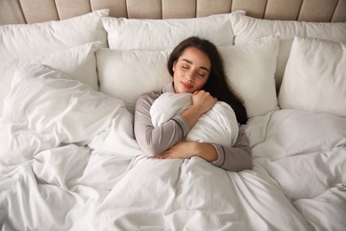Photo of Beautiful young woman wrapped with soft blanket sleeping in bed at home, above view