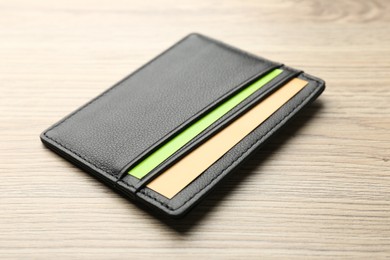 Leather business card holder with colorful cards on wooden table, closeup