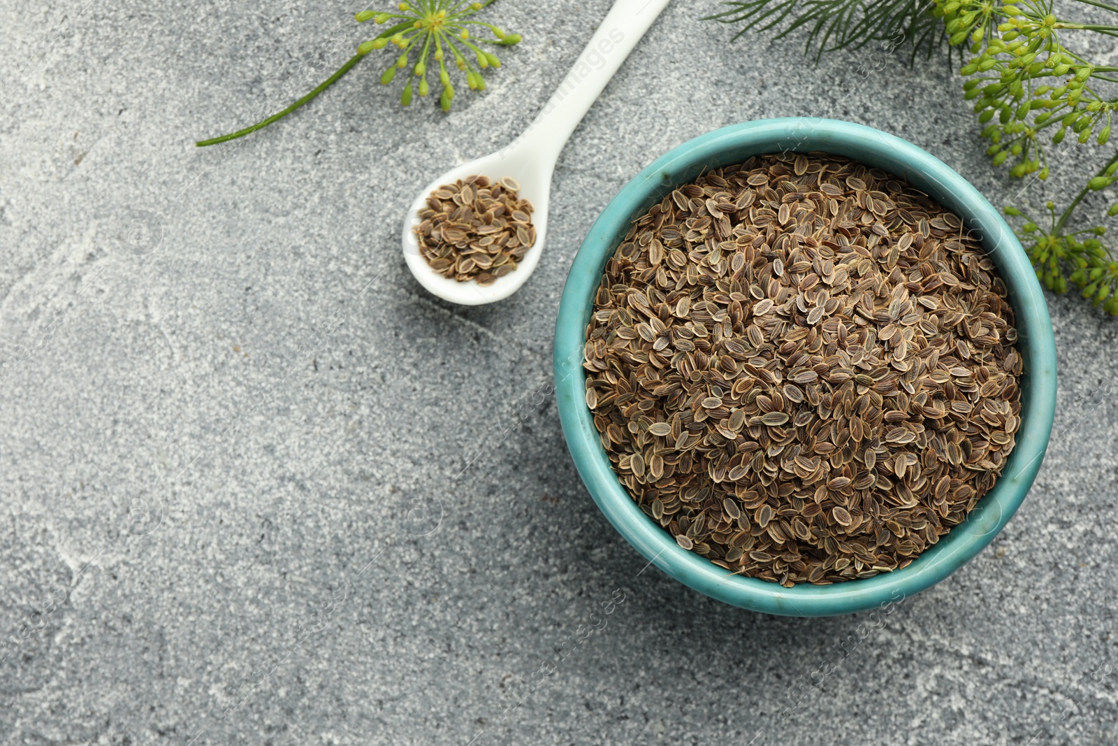 Photo of Bowl of dry seeds, spoon and fresh dill on grey table, flat lay. Space for text