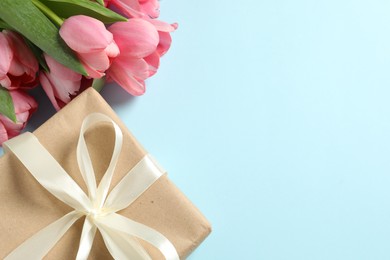 Photo of Happy Mother's Day. Beautiful pink tulips and gift box on light blue background, flat lay. Space for text