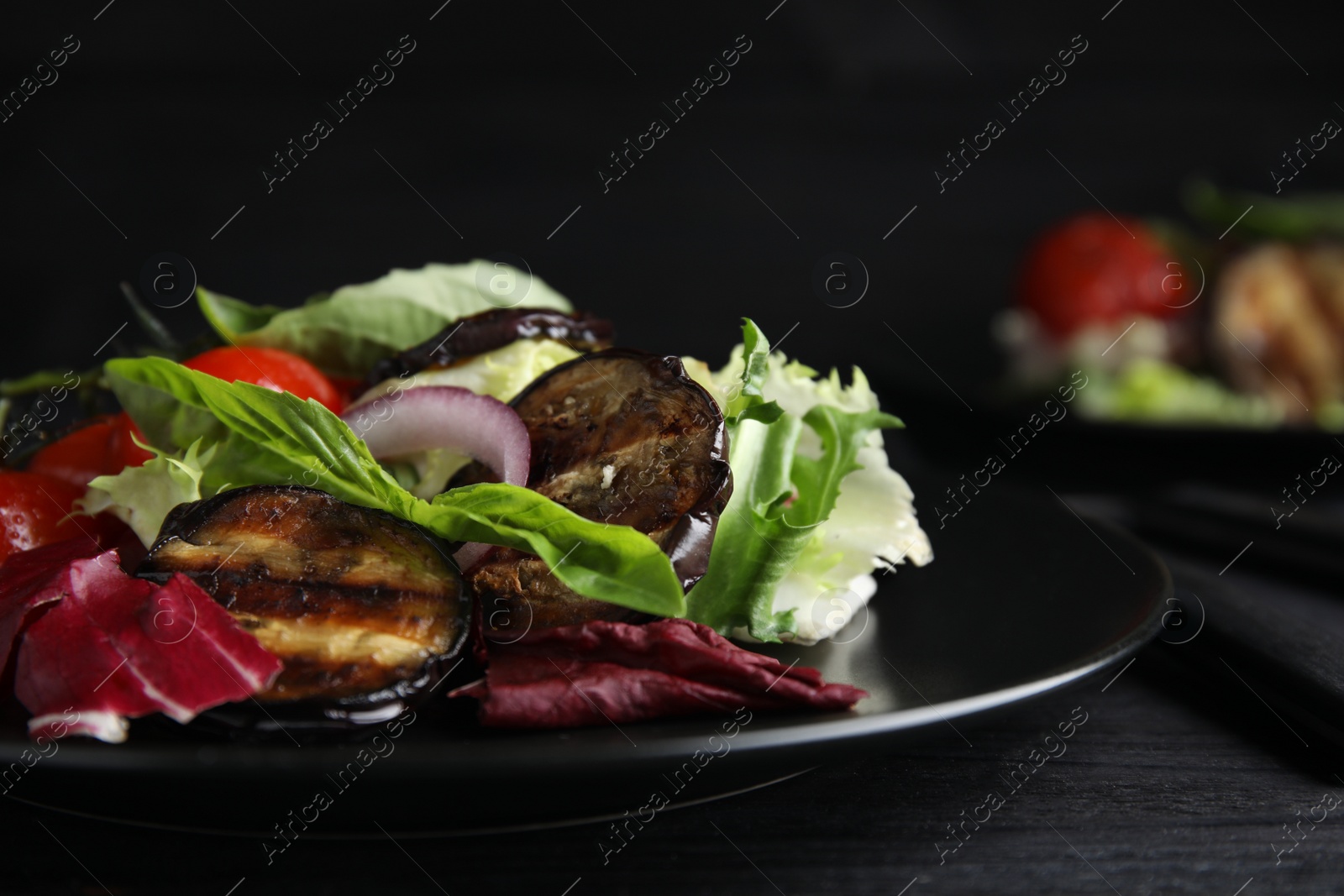 Photo of Delicious salad with roasted eggplant and basil served on black wooden table, closeup