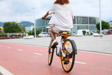 Photo of Young woman riding bicycle on lane in city, back view