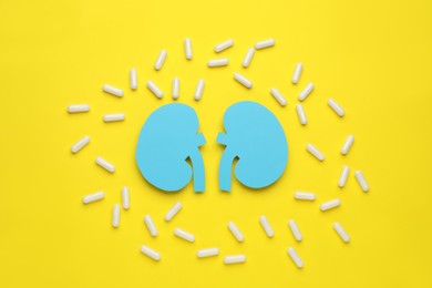 Paper cutout of kidneys and pills on yellow background, flat lay
