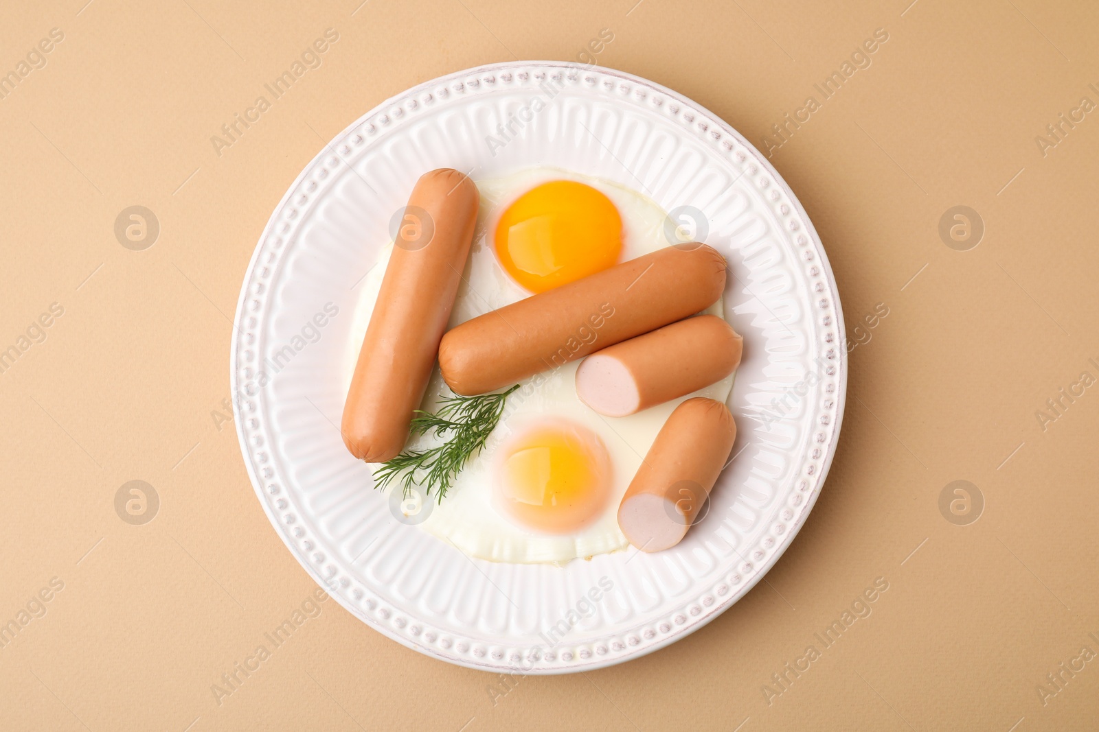 Photo of Delicious boiled sausages, fried eggs and dill on beige background, top view