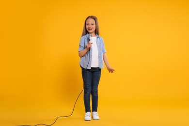 Photo of Cute little girl with microphone singing on yellow background