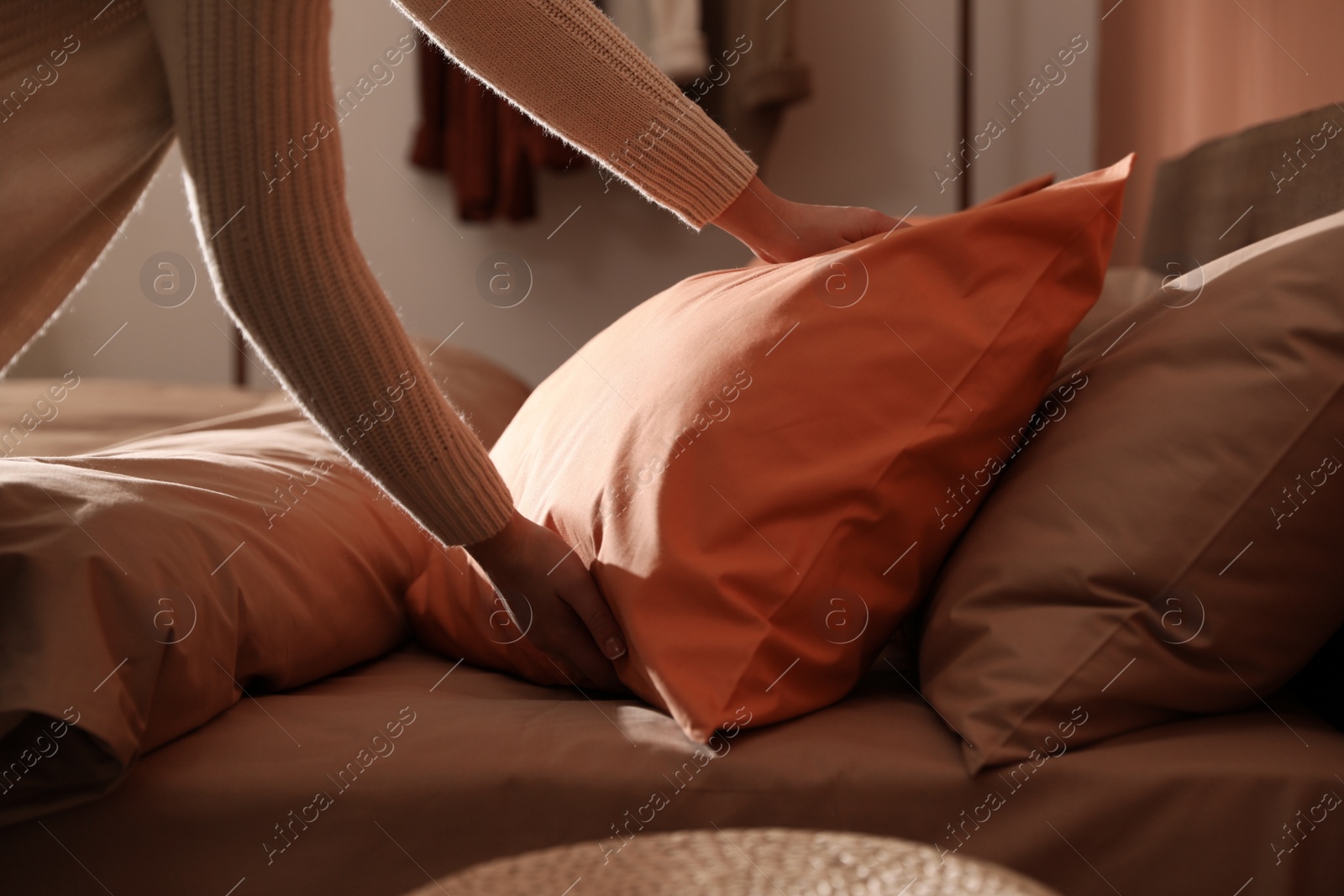 Photo of Woman making bed with fresh linens and orange pillow, closeup