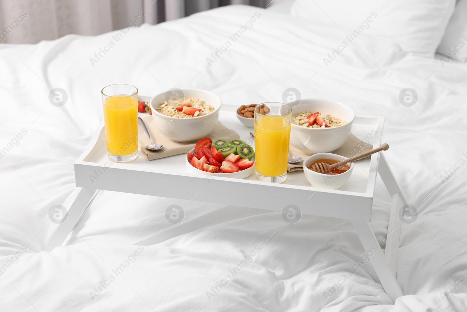 Tasty breakfast served in bed. Oatmeal, juice, fruits, almonds and honey on tray Photo of Tasty breakfast served in bed. Oatmeal, juice, fruits, almonds and honey on tray