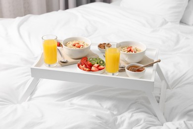 Photo of Tasty breakfast served in bed. Oatmeal, juice, fruits, almonds and honey on tray