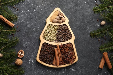 Photo of Different spices, nuts and fir branches on dark gray textured table, flat lay