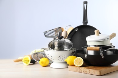 Set of clean kitchenware and lemons on wooden table against light background. Space for text
