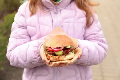 Little girl holding fresh delicious burger outdoors, closeup. Street food