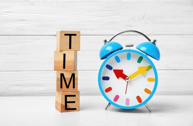 Alarm clock and cubes with word TIME on table