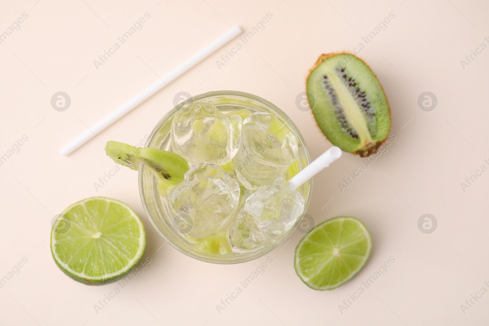 Photo of Glass of refreshing drink, cut kiwi and lime on beige background, flat lay