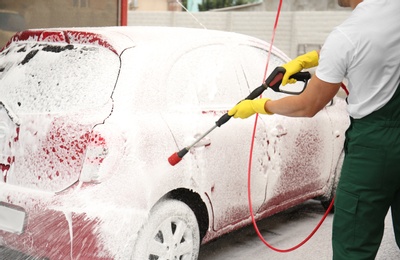 Photo of Male worker cleaning vehicle with high pressure foam jet at car wash