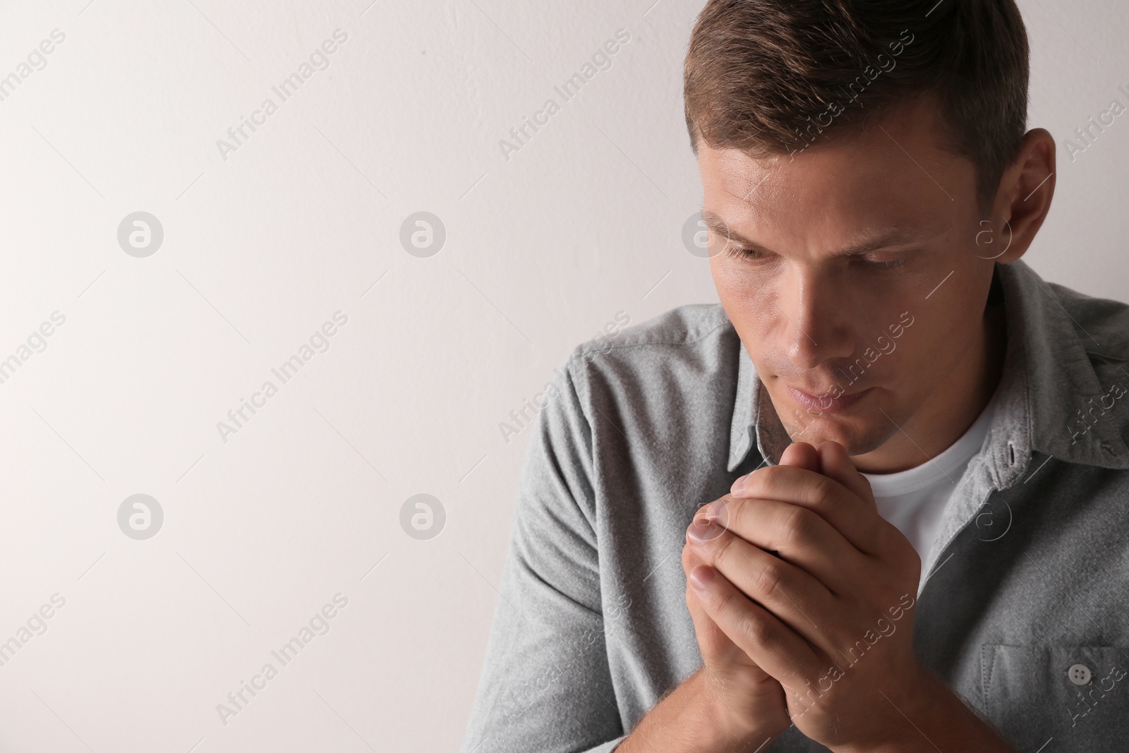 Photo of Man with hands clasped together for prayer on light background. Space for text