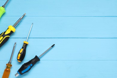 Group of different screwdrivers on light blue wooden table, top view