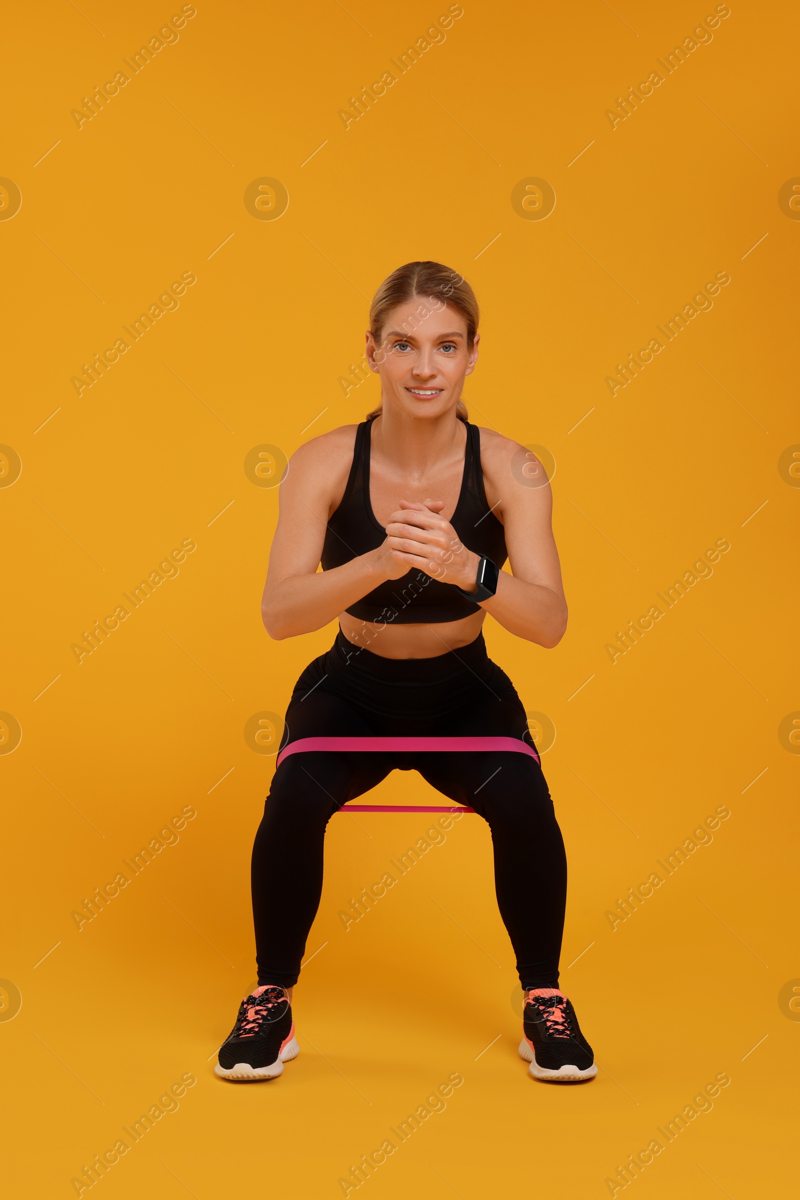 Photo of Woman exercising with elastic resistance band on orange background