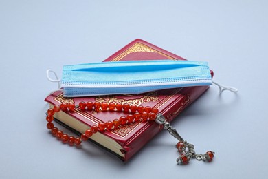 Muslim prayer beads, Quran and medical mask on light background