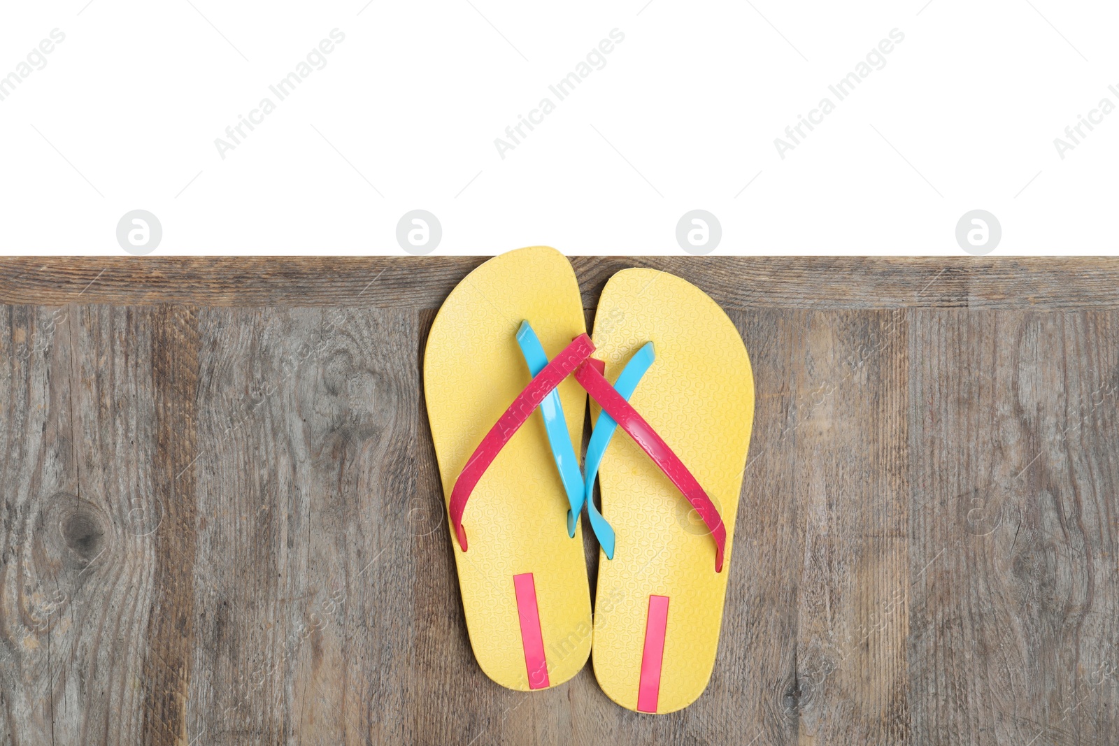 Photo of Pair of yellow flip flops on wooden table against white background, top view