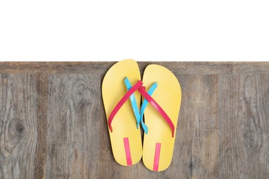 Pair of yellow flip flops on wooden table against white background, top view
