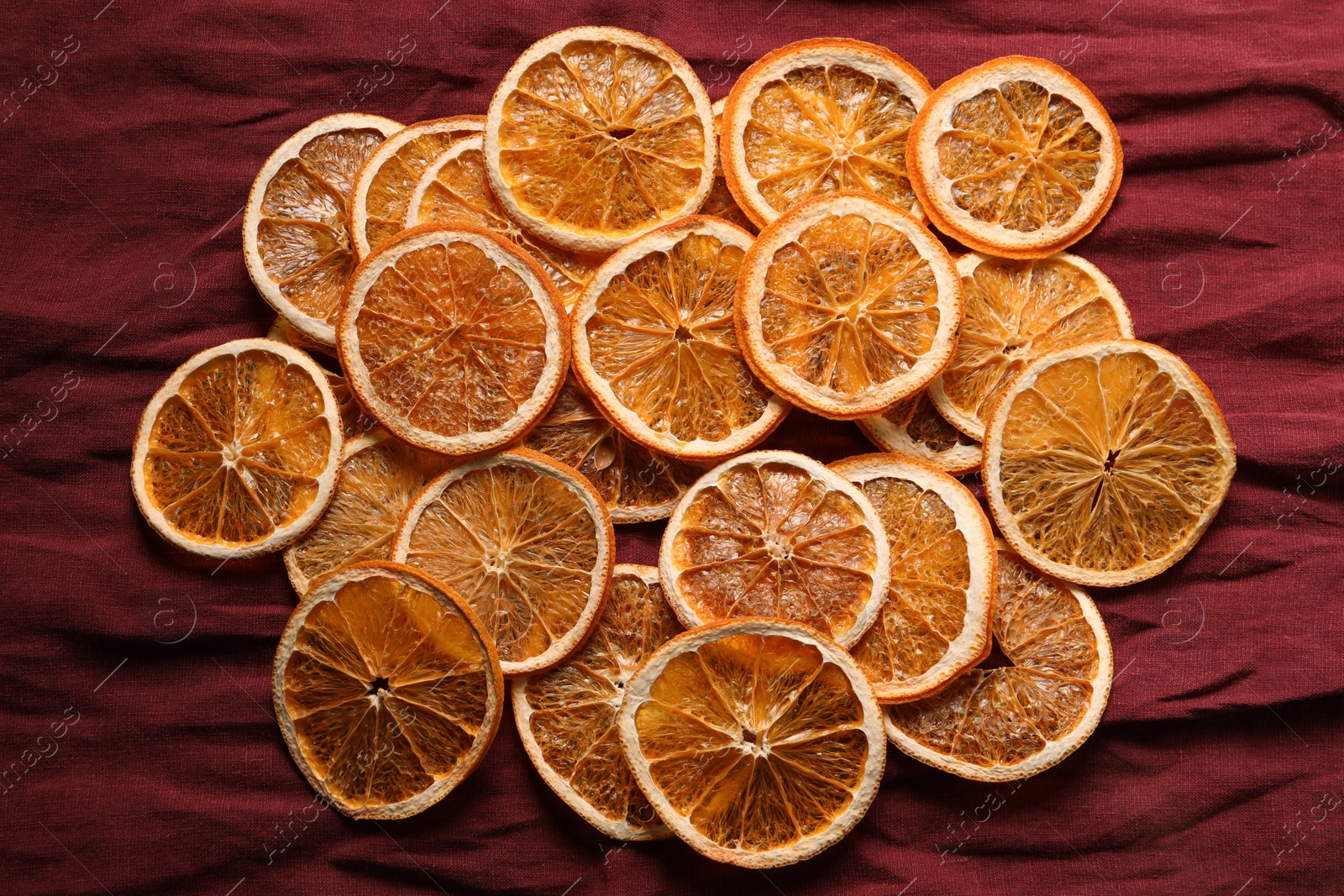 Photo of Heap of dry orange slices on burgundy fabric, flat lay