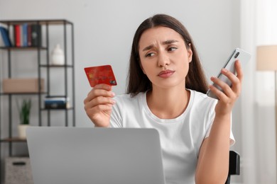 Photo of Confused woman with credit card, smartphone and laptop at home. Be careful - fraud