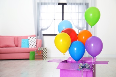 Photo of Gift box with bright air balloons in living room. Space for text