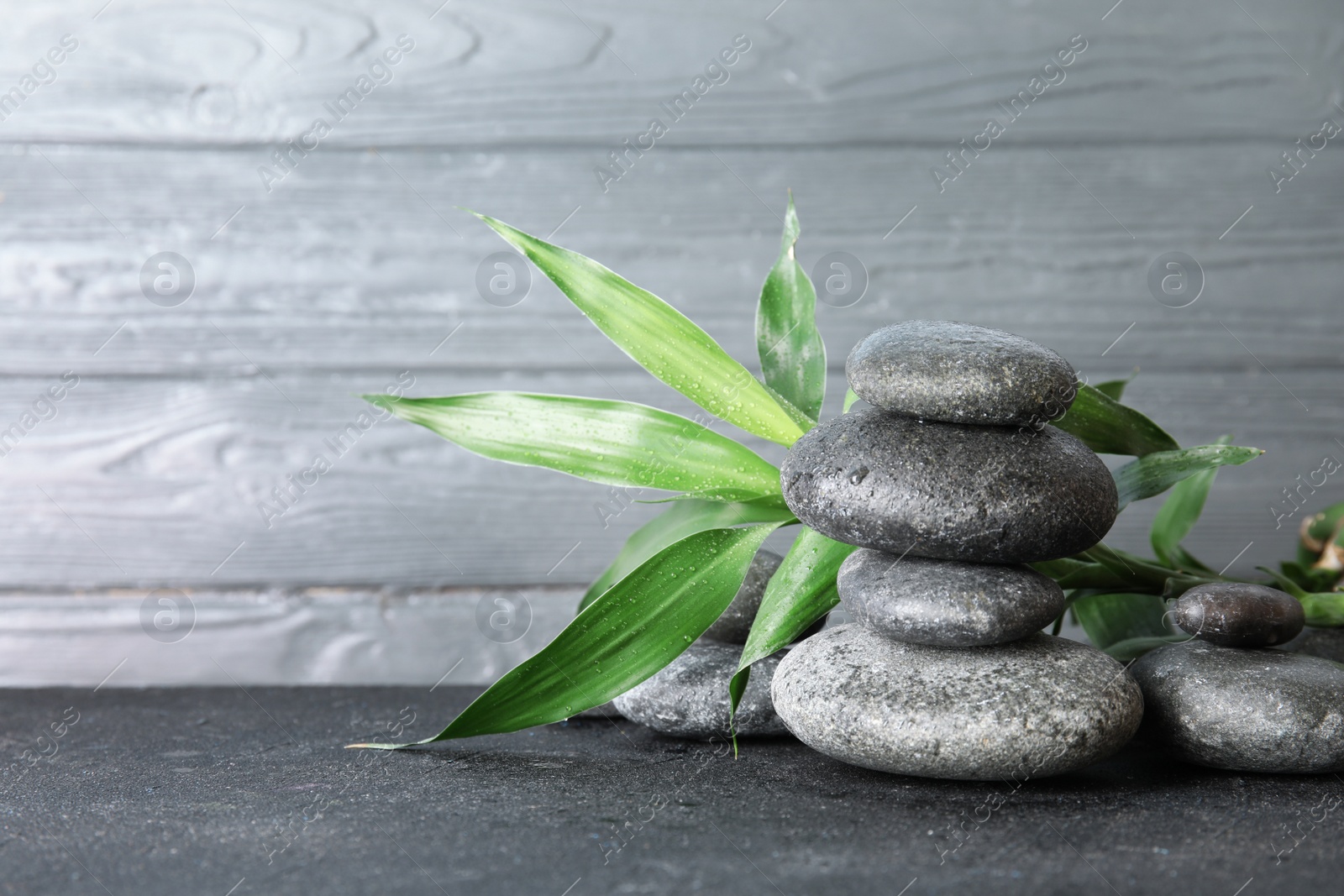 Photo of Stacked zen stones and bamboo leaves on table against wooden background. Space for text